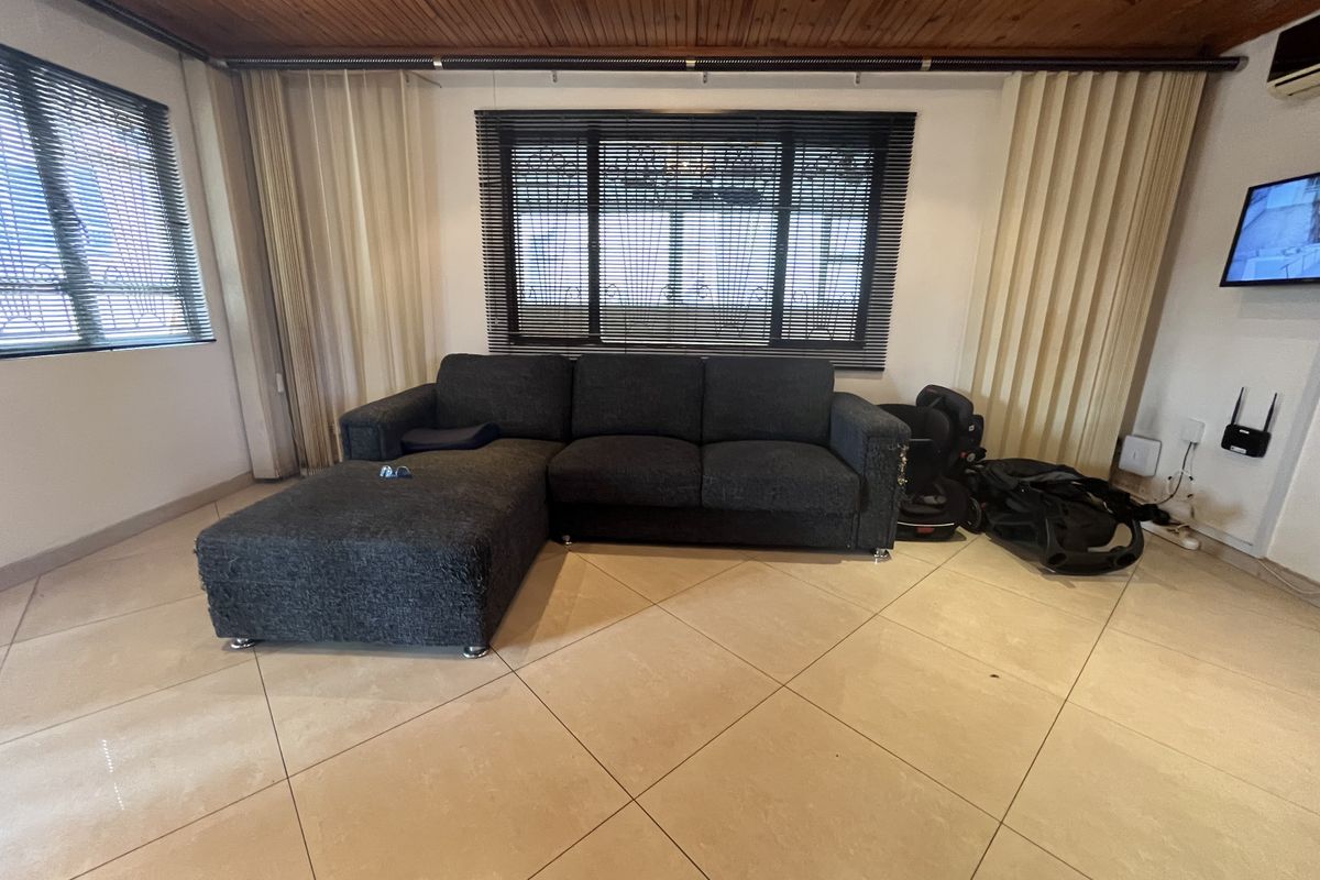 A spacious living room featuring large format floor tiles, a timber-clad ceiling, and large windows with fitted blinds.