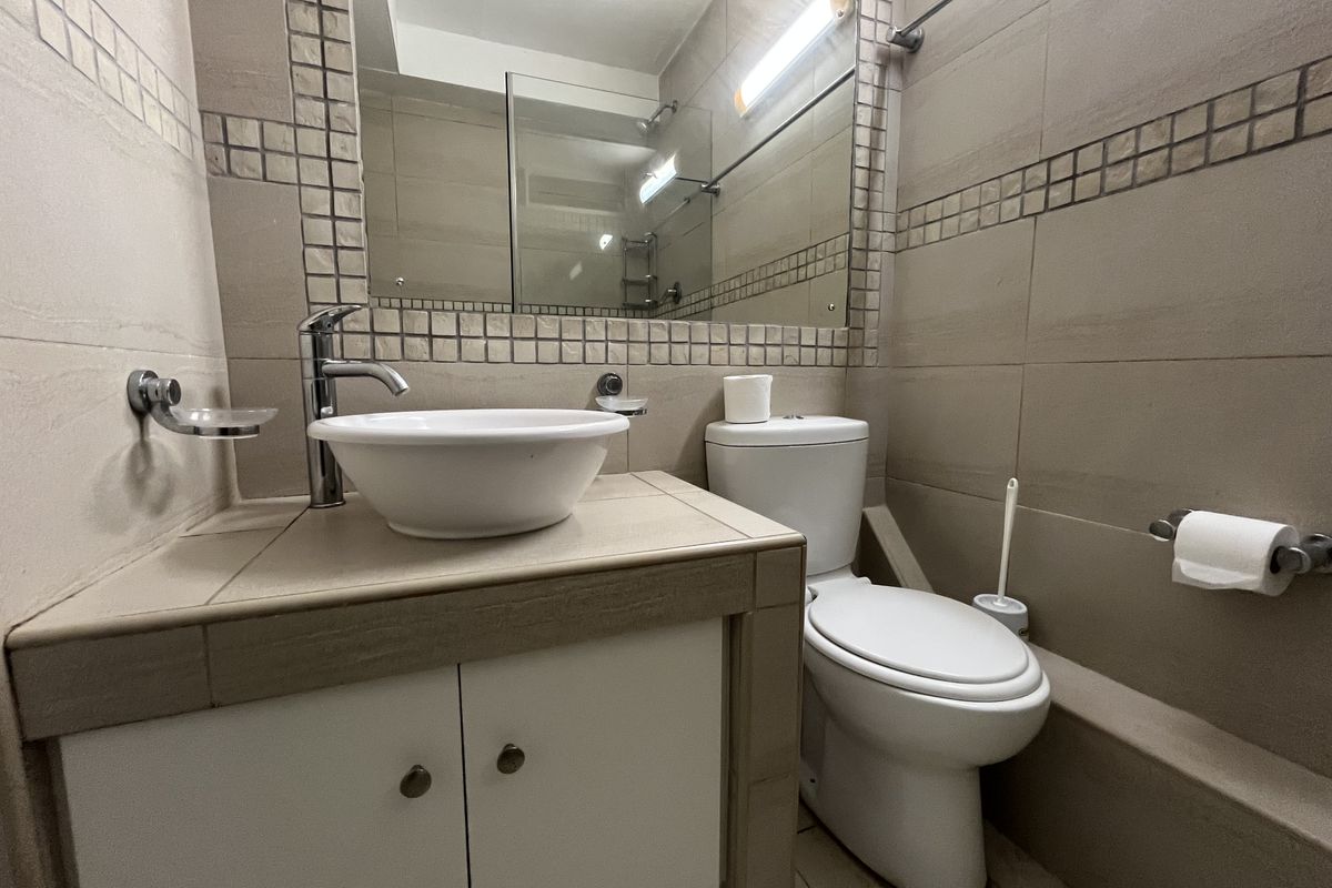 A compact bathroom featuring a modern vessel sink, vanity cabinet, wall-mounted mirror, and a standard toilet with tiled wall finishes.