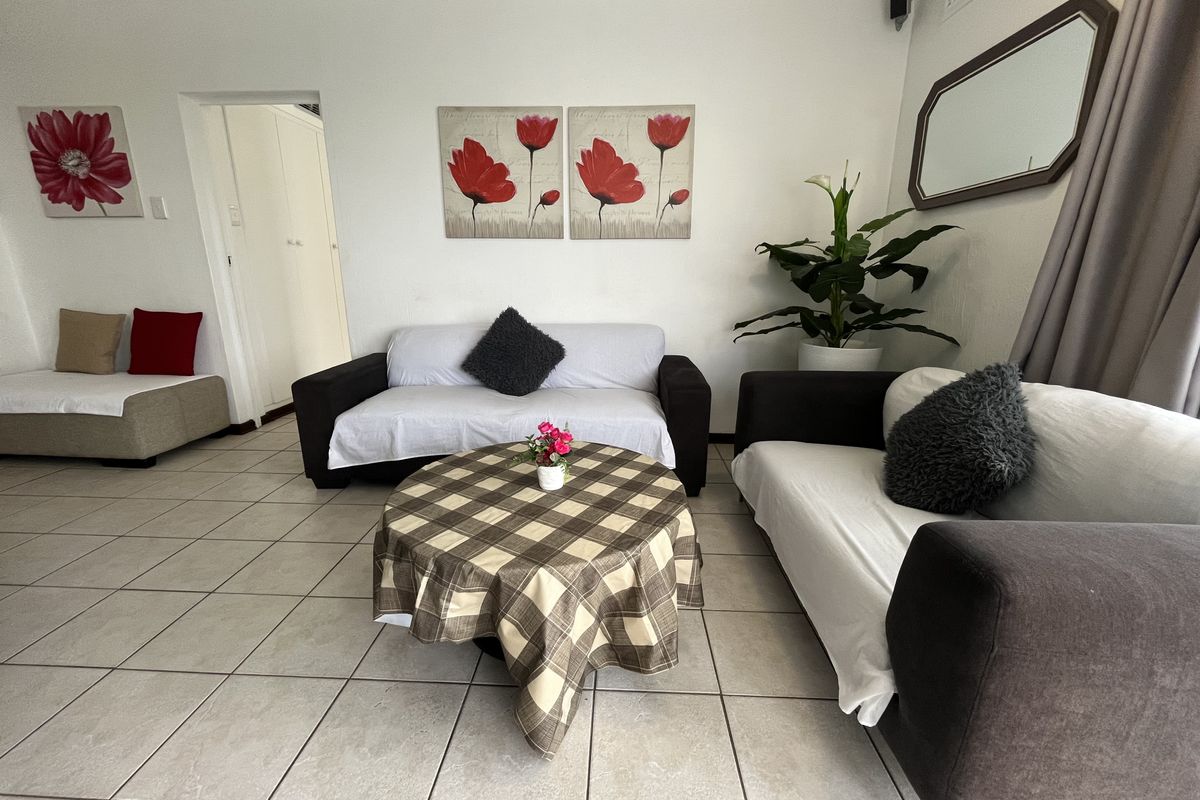 A living room featuring neutral ceramic floor tiles and access to an adjacent hallway.