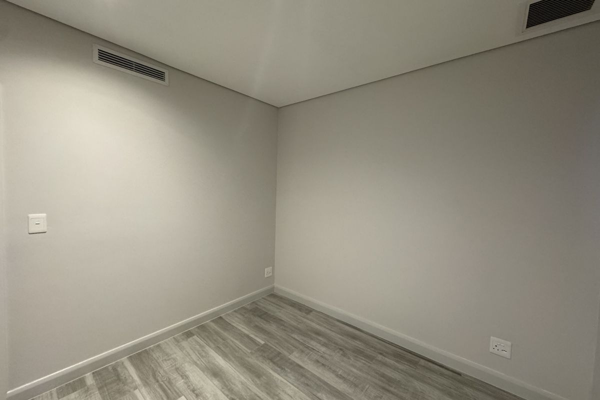 A clean, empty bedroom featuring neutral walls, modern wood-look flooring, recessed ceiling lighting, and integrated air conditioning vents.