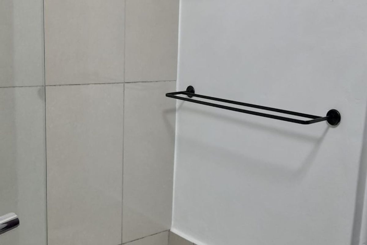 A clean bathroom area featuring a bathtub, glass shower screen, wall-mounted glass shelf, and a modern black towel rail.