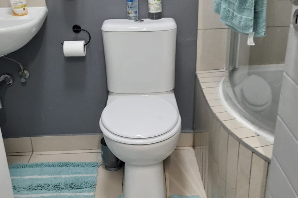 A compact bathroom featuring a white toilet, wall-mounted basin, and a tiled shower enclosure with a curved glass door.
