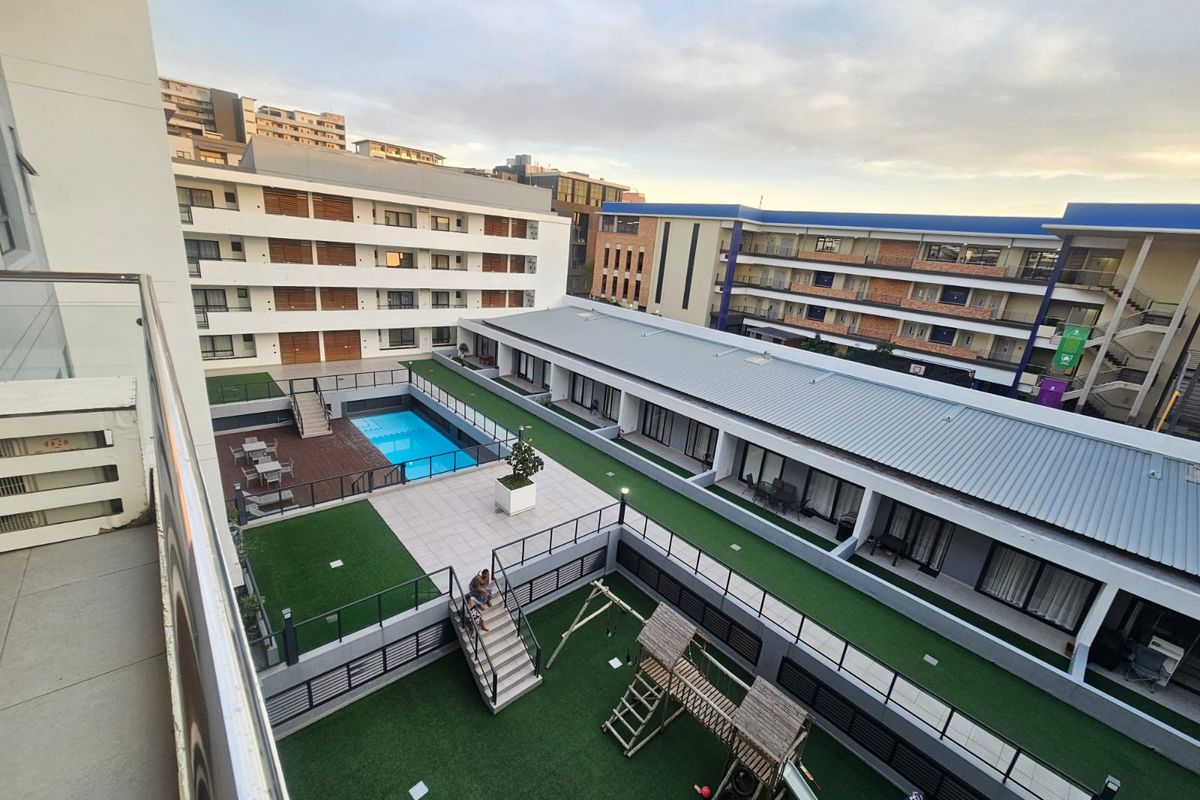 Elevated view of the apartment complex courtyard featuring a swimming pool, landscaped artificial grass areas, and a children's play structure.