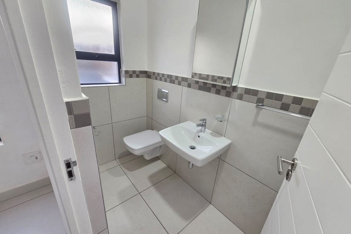 A clean and modern guest bathroom featuring a wall-mounted toilet, a sleek basin, and neutral tiled finishes.