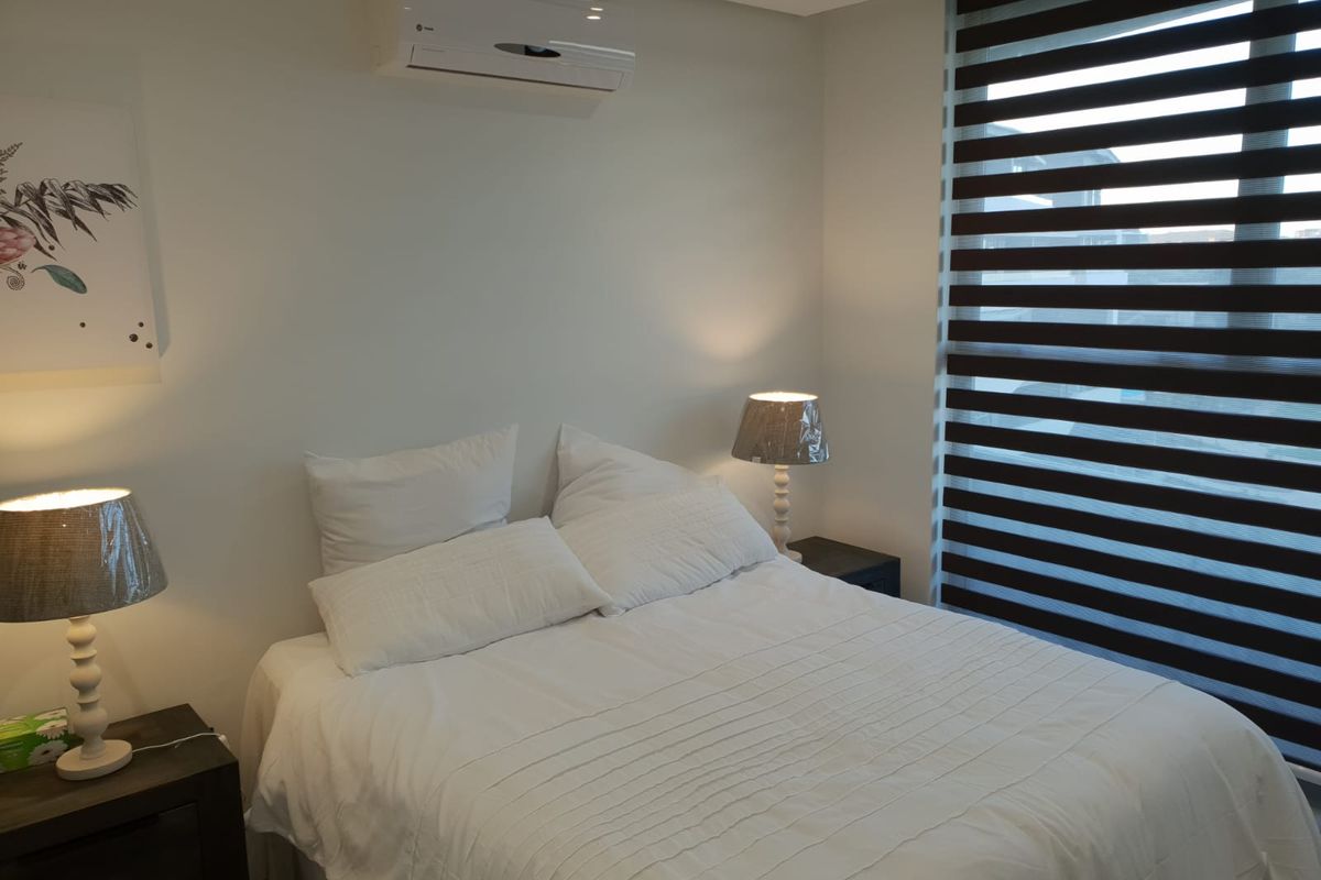 A well-maintained bedroom featuring a wall-mounted air conditioning unit and modern zebra-style window blinds.