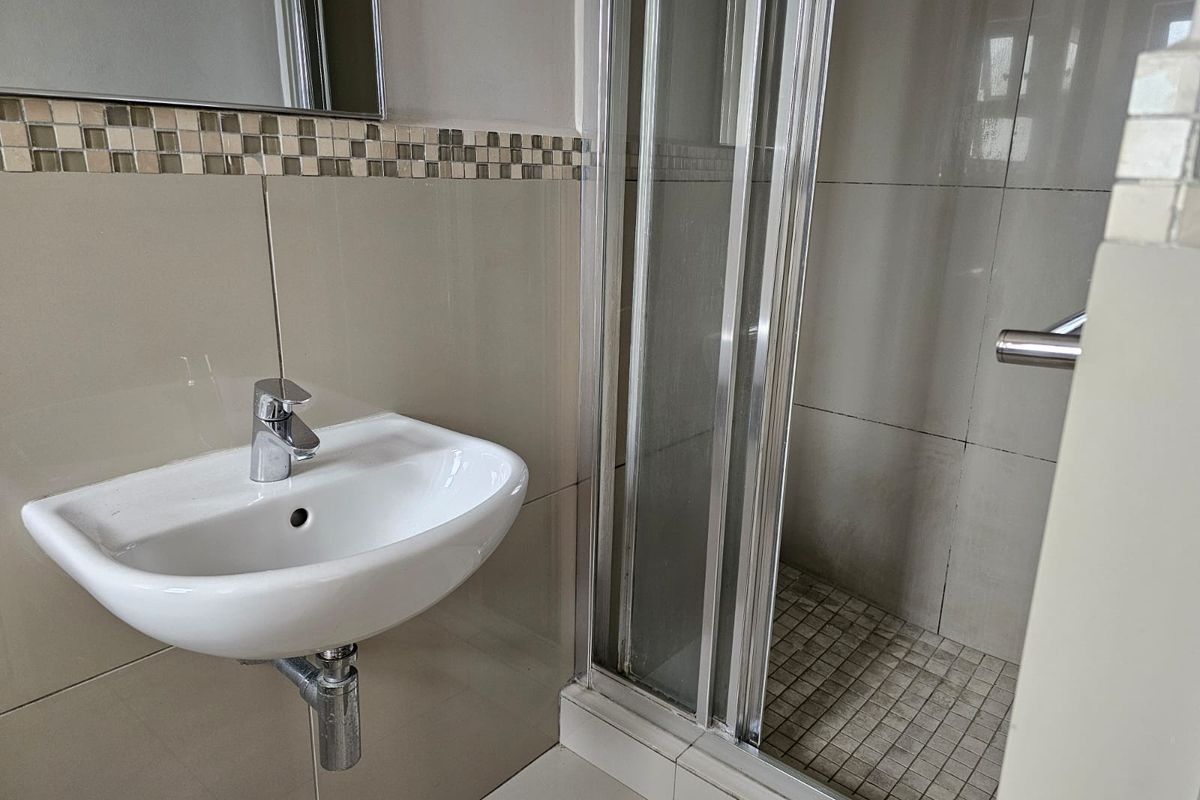 A functional bathroom featuring a wall-mounted basin, chrome mixer tap, and a glass-enclosed shower with neutral wall tiling and mosaic accents.