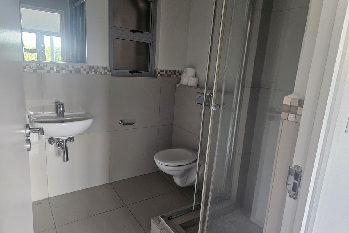 A modern bathroom featuring a wall-mounted toilet, a glass-enclosed shower, and a wall-hung basin with neutral tiled finishes.