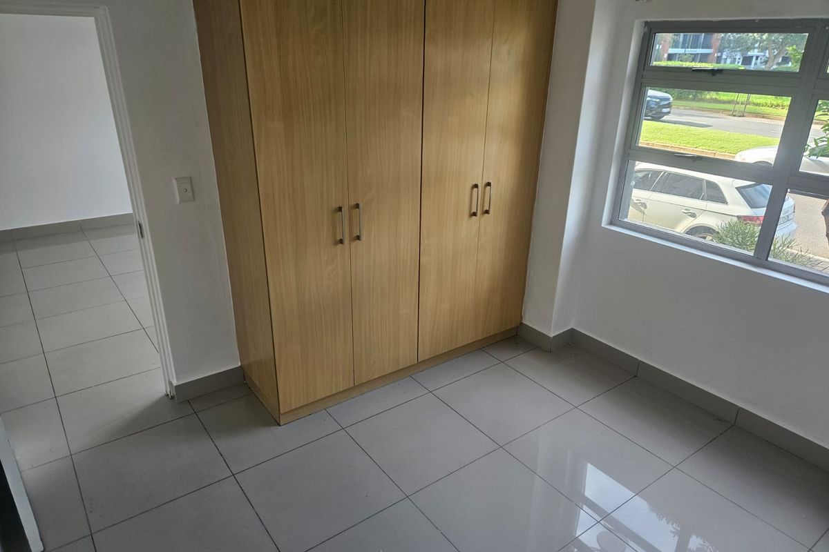 A bright, empty bedroom featuring neutral floor tiles and built-in wooden cabinetry, offering a clean and versatile space.