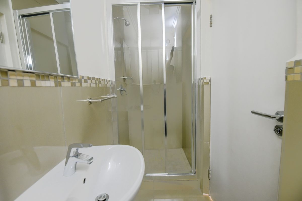 A functional bathroom featuring a glass-enclosed shower, a wall-mounted basin with chrome faucet, and neutral wall tiling with a decorative mosaic border.