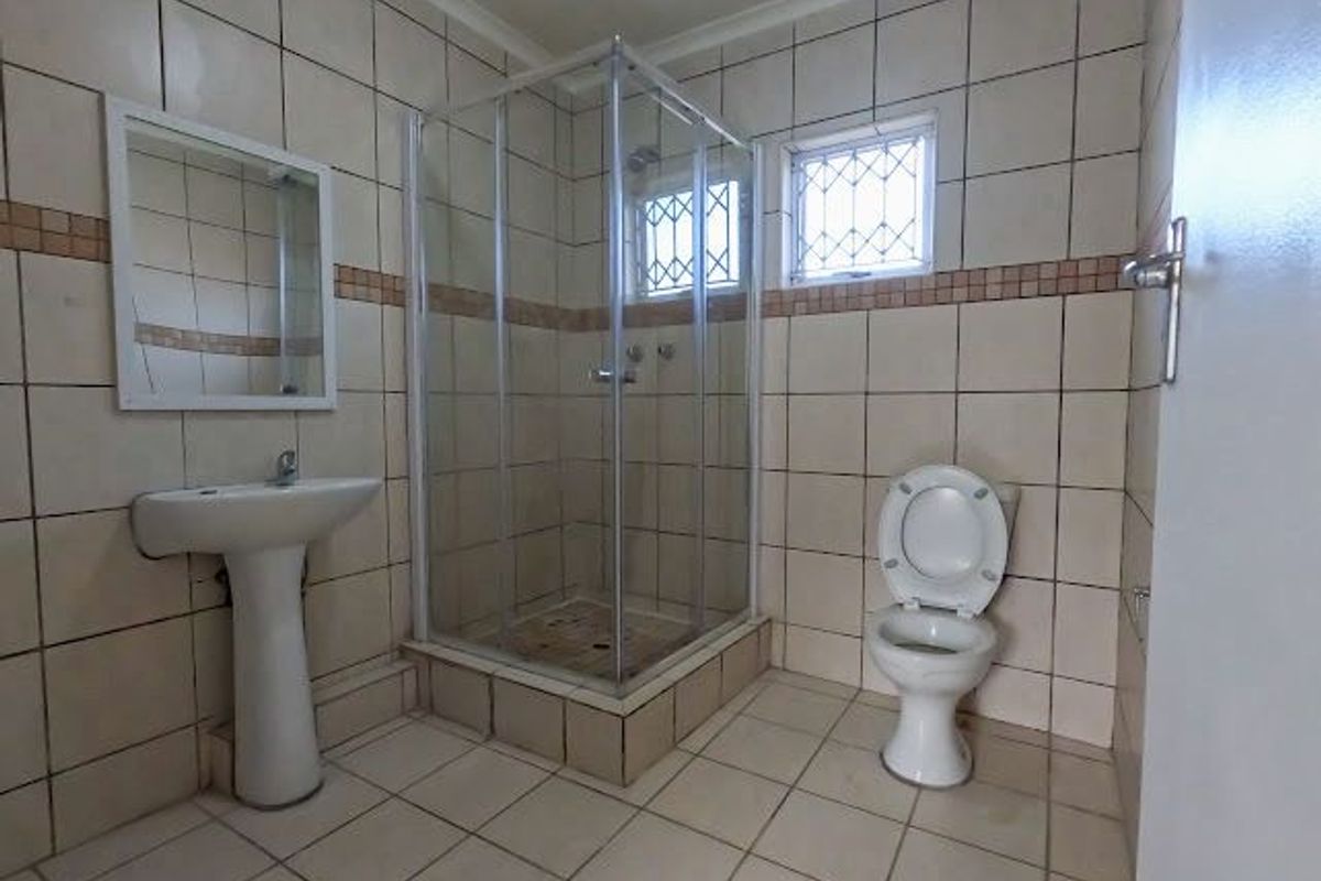 A functional bathroom featuring a corner shower enclosure, pedestal basin, and toilet with neutral floor-to-ceiling wall tiling.