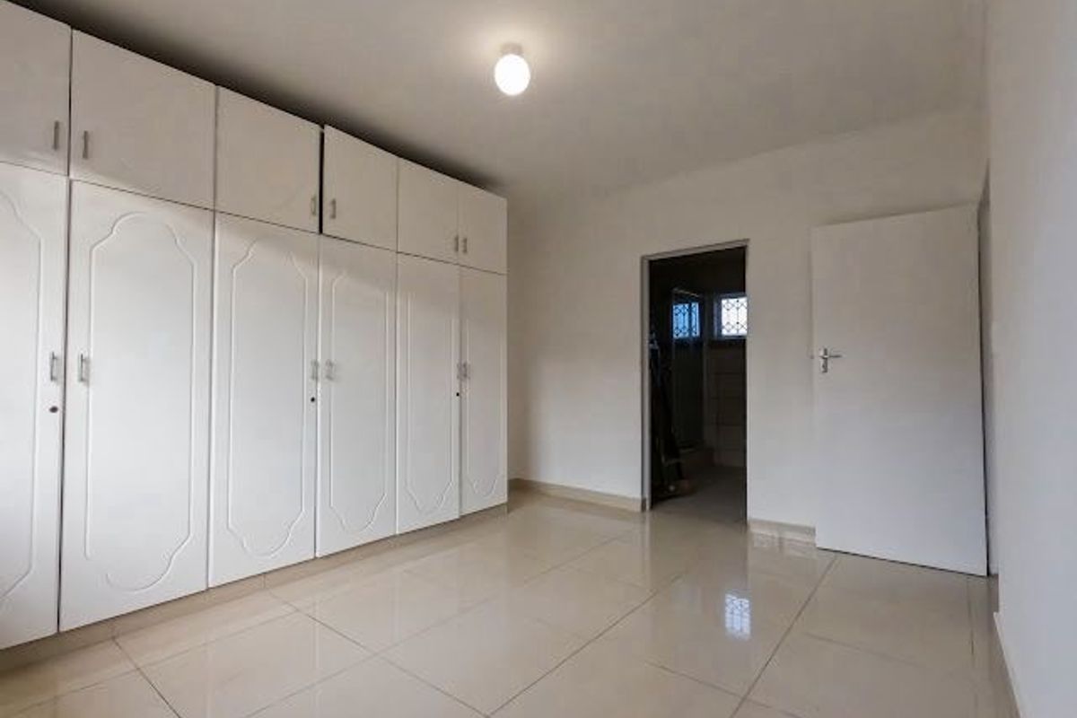 A bright, empty bedroom featuring extensive built-in white cabinetry, tiled flooring, and a doorway leading to an adjacent space.