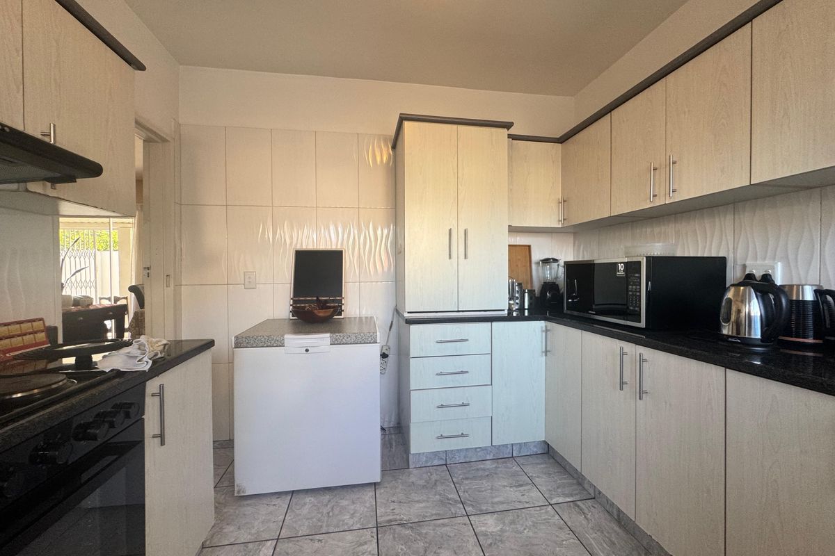 A functional kitchen featuring light wood-grain cabinetry, dark granite countertops, tiled splashbacks, and tiled flooring, providing ample storage and workspace.
