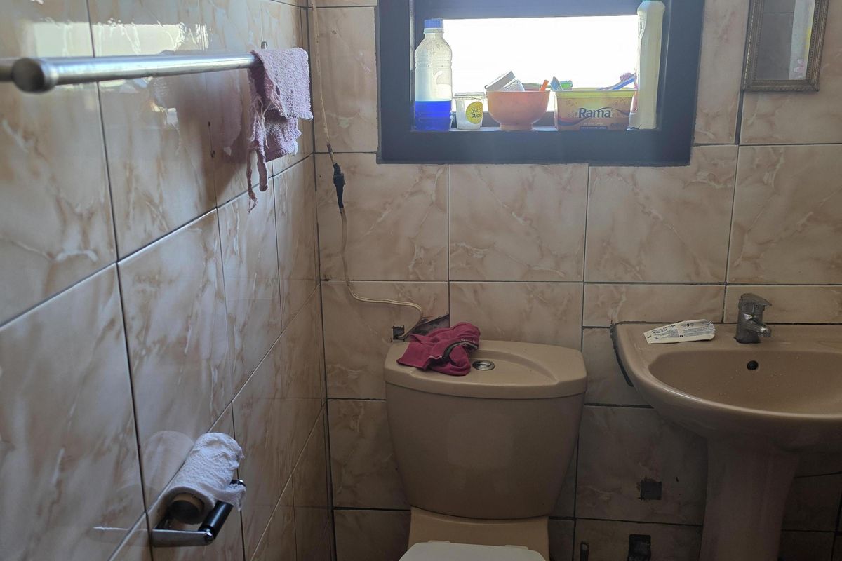 A compact bathroom featuring a pedestal basin, toilet, and floor-to-ceiling tiled walls with a window for natural light.