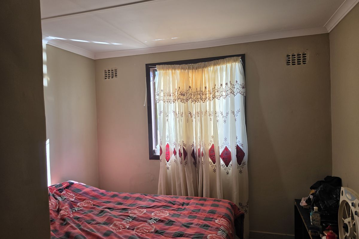 A standard bedroom featuring neutral wall tones, a window with curtain fixtures, and integrated wall ventilation vents.