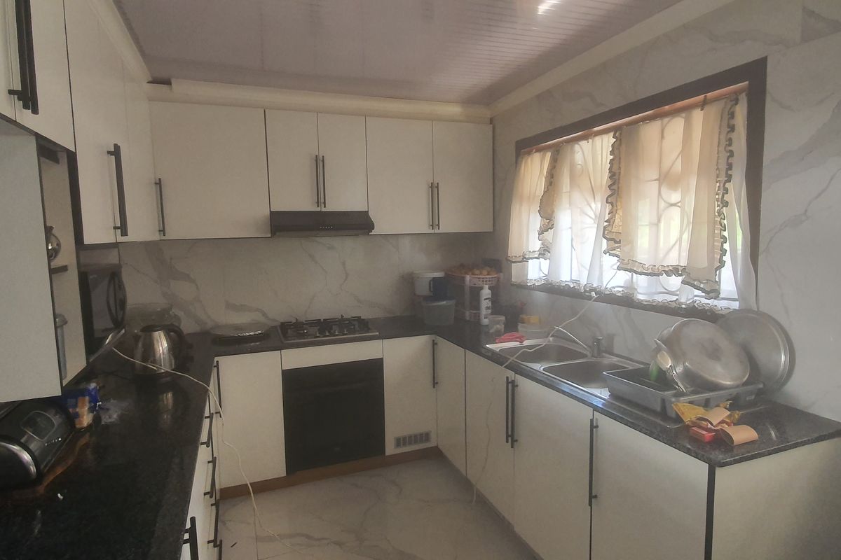 A functional kitchen featuring white cabinetry, dark granite countertops, a built-in oven, gas hob, and a double sink with marble-look wall tiling.