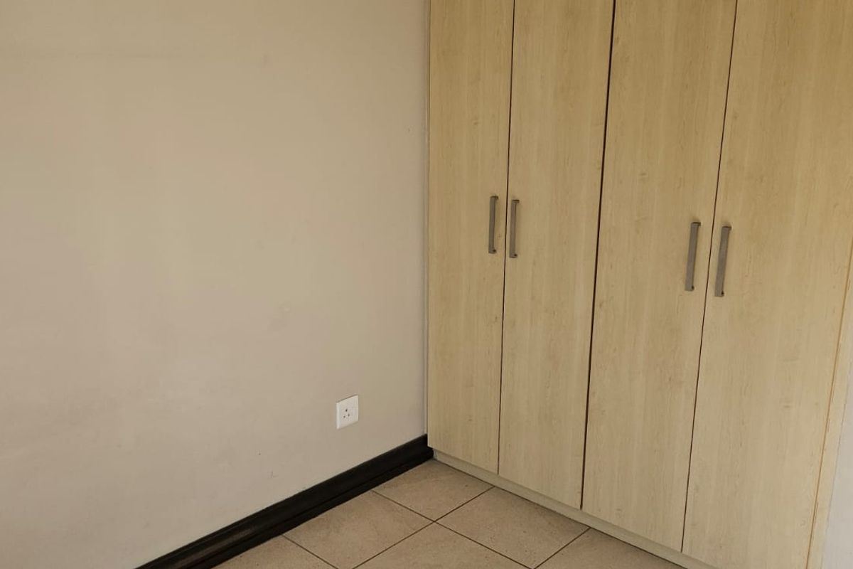 A bedroom interior featuring built-in light wood-finish cupboards and tiled flooring.