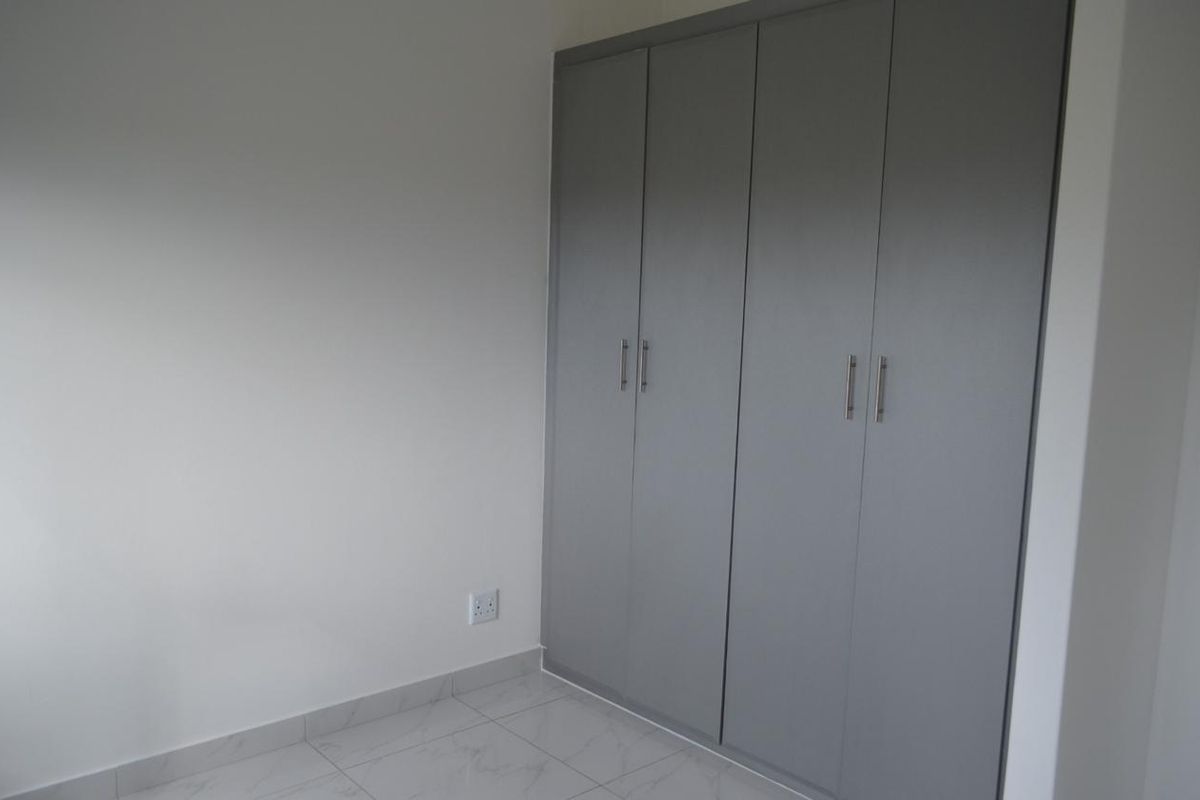 A clean, modern bedroom featuring neutral grey built-in cupboards and light-colored tiled flooring.