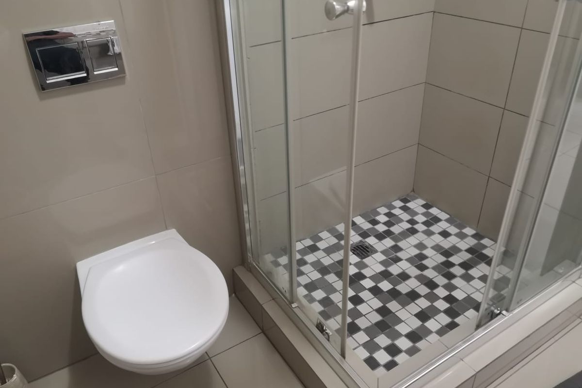Modern bathroom featuring a wall-mounted toilet with a chrome flush plate and a glass-enclosed shower with a decorative checkered tile floor.