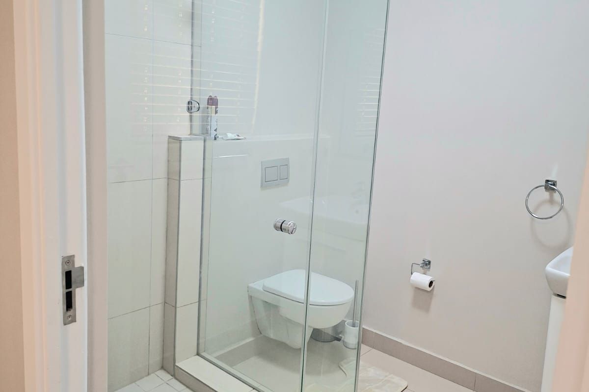 A modern bathroom featuring a glass-enclosed shower, wall-mounted toilet with concealed cistern, and tiled flooring.