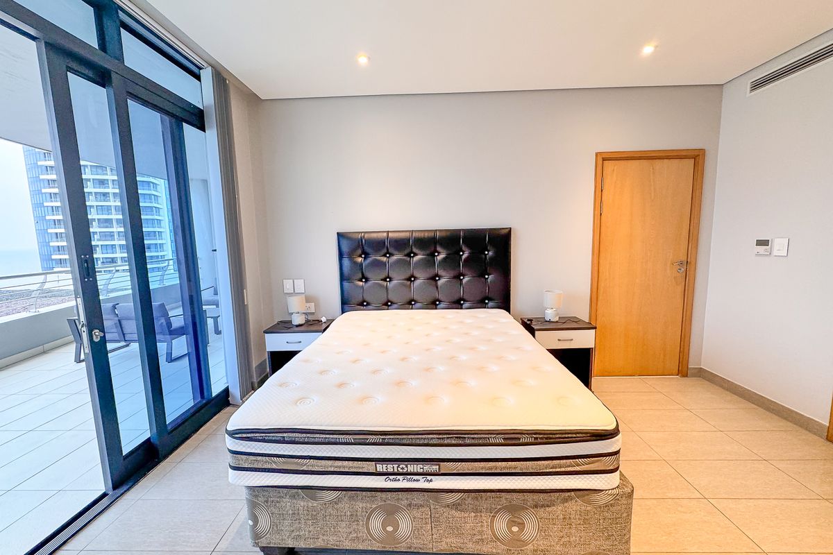 Spacious bedroom featuring large sliding glass doors leading to a private balcony, neutral tiled flooring, and recessed ceiling lighting.