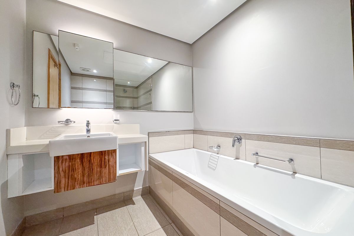 Modern bathroom featuring a wall-mounted vanity with integrated basin, large wall mirrors, and a tiled bathtub with chrome fixtures.