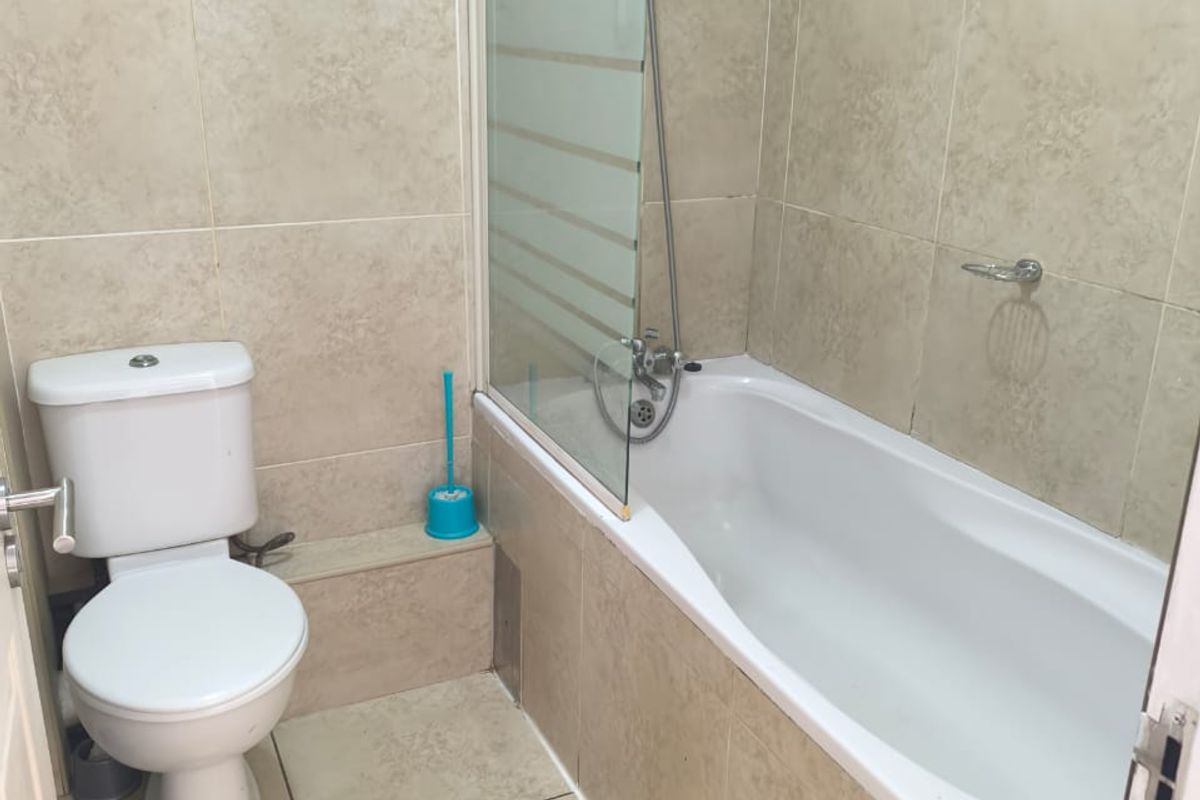 A functional bathroom featuring a bathtub with a glass shower screen, tiled walls and flooring, and a standard toilet.