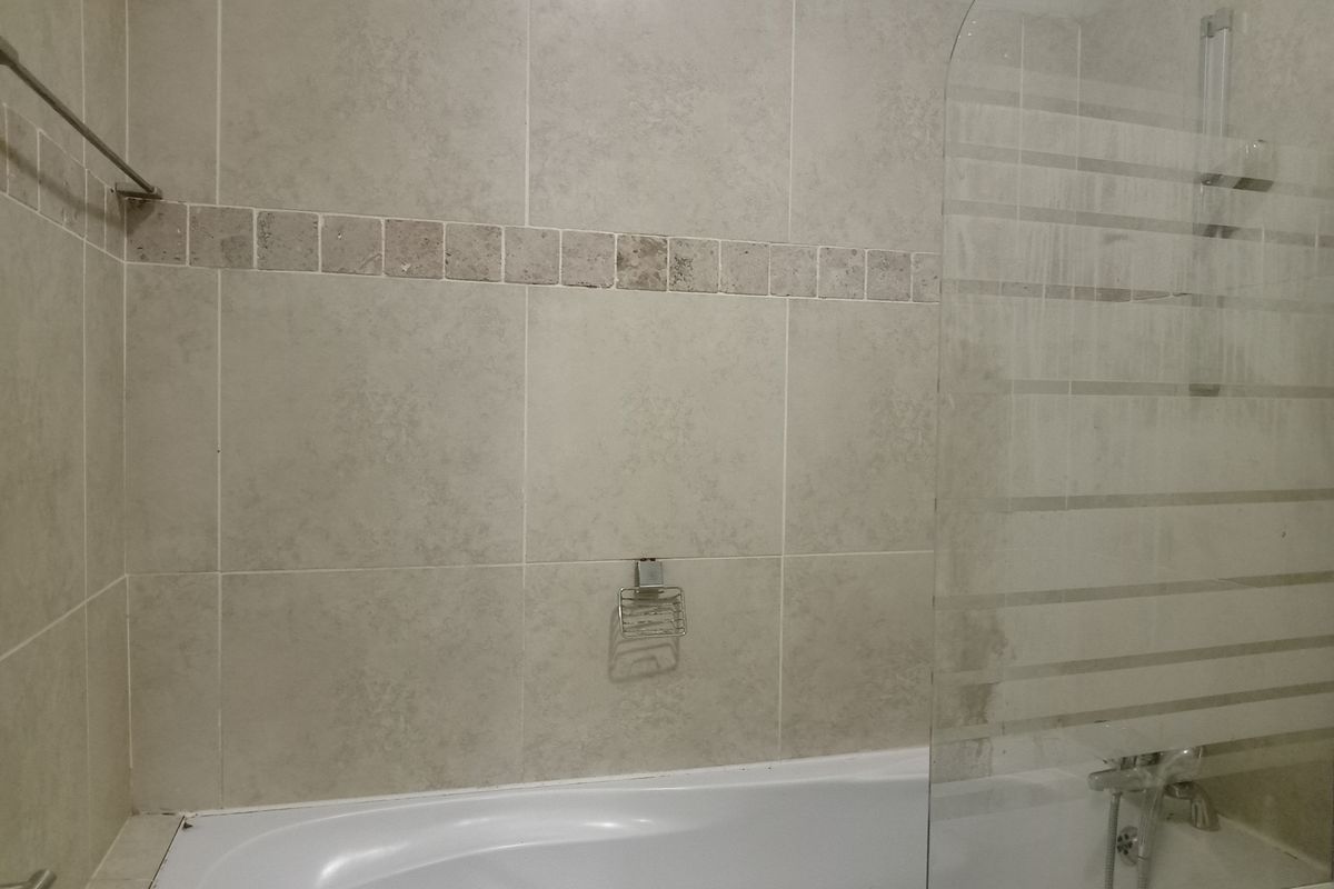 A functional bathroom featuring a bathtub with a glass shower screen, tiled walls with a decorative border, and integrated chrome fixtures.