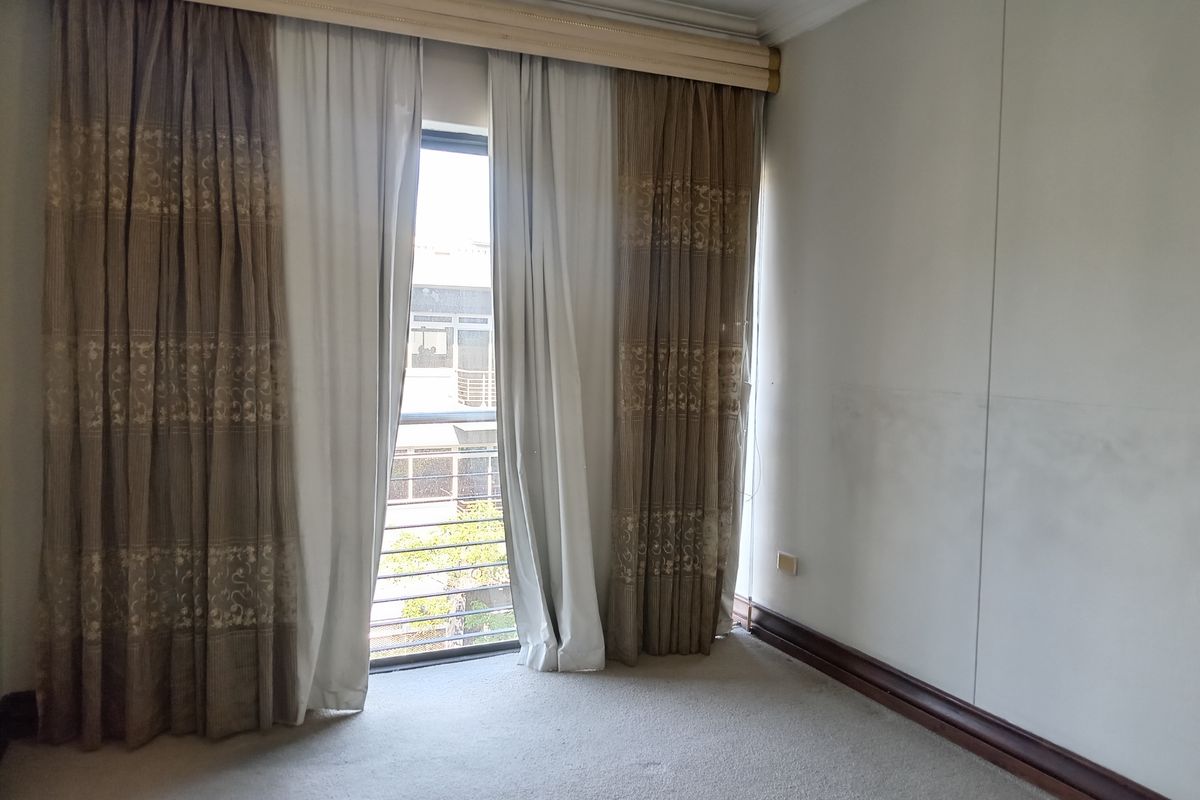 An empty bedroom featuring neutral carpeting, wall-mounted curtain tracks, and a window with security bars overlooking the exterior.