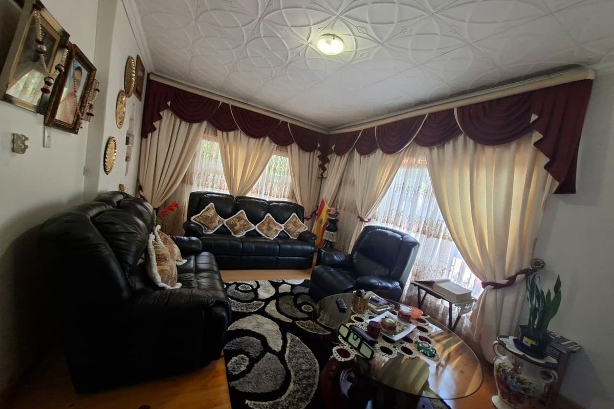 A living room featuring timber flooring and a decorative patterned ceiling, with large windows dressed in traditional heavy drapery.