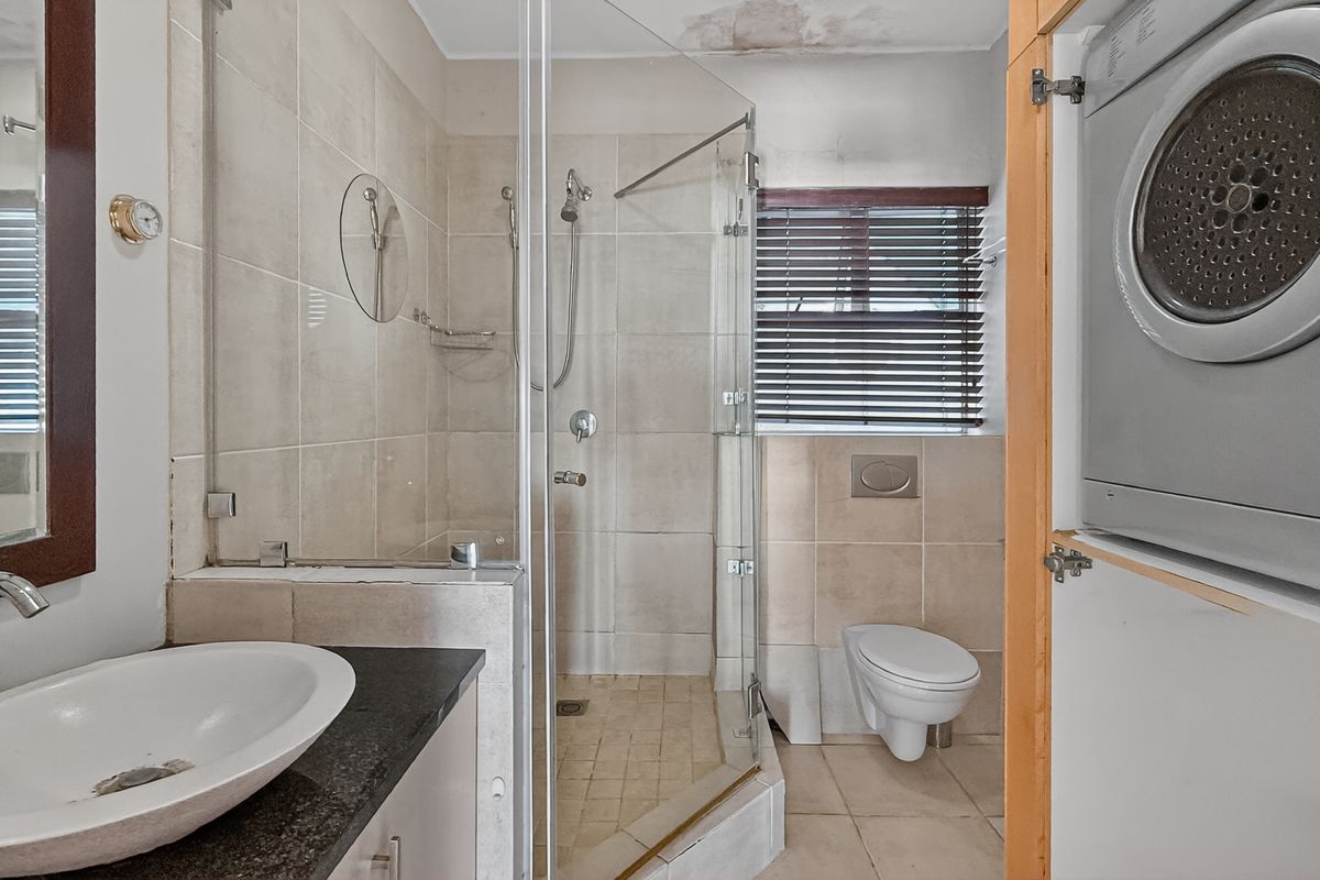 A compact bathroom featuring a glass-enclosed shower, wall-mounted toilet, vanity basin, and a built-in laundry cupboard with a dryer.