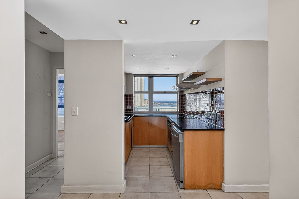 A functional kitchen featuring wooden cabinetry, dark countertops, tiled backsplash, and integrated appliances, with a view through the window.