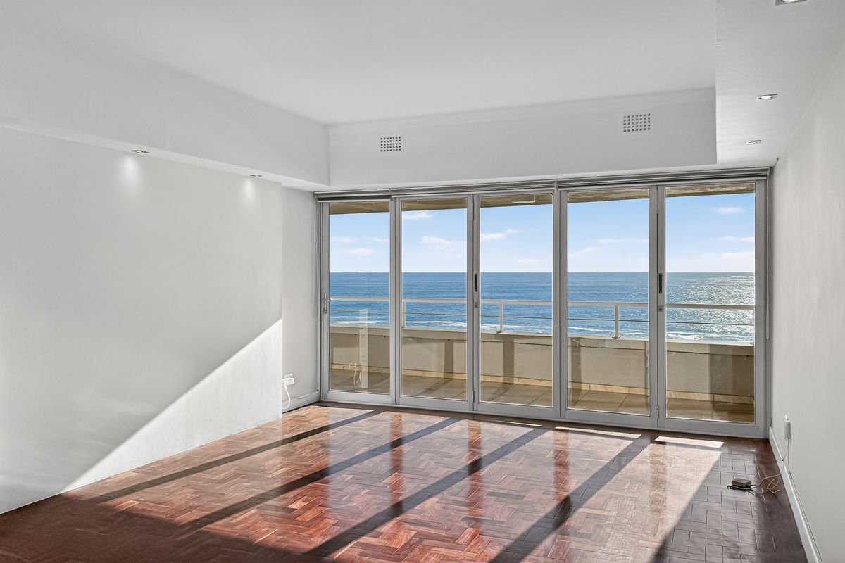 Bright and spacious living area featuring classic parquet flooring and large sliding glass doors that open onto a balcony with stunning ocean views.