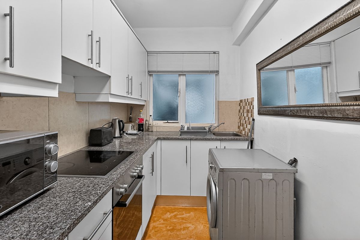 Compact kitchen featuring white cabinetry, granite countertops, built-in oven, hob, and integrated sink with a window for natural light.