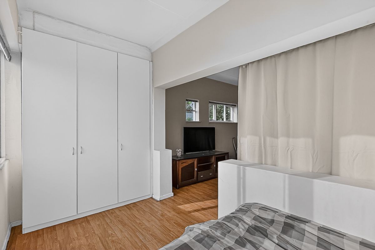 A bedroom featuring built-in wardrobes, laminate flooring, and an open-plan layout connecting to an adjacent living area.