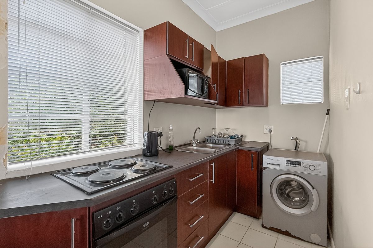 Compact kitchen featuring dark wood cabinetry, integrated electric hob and oven, stainless steel sink, and dedicated space for a washing machine.