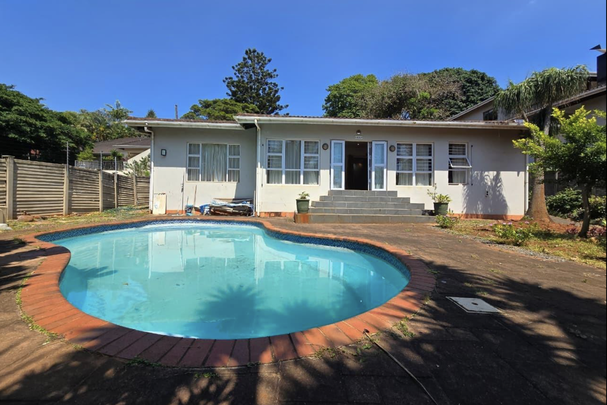 Rear view of the property featuring a swimming pool with brick coping, paved patio area, and direct access to the home via concrete steps.
