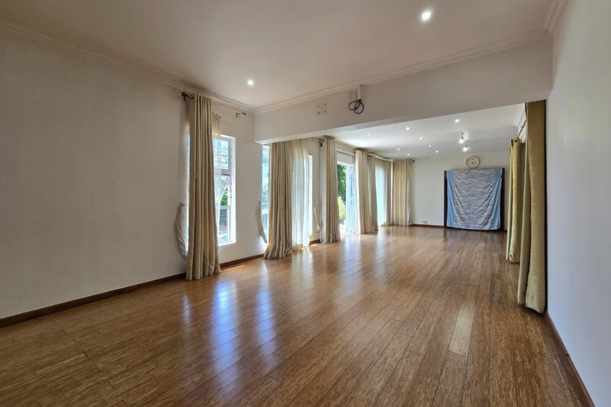 Spacious, light-filled living area featuring polished laminate timber flooring, recessed downlighting, and multiple sliding glass doors providing access to the exterior.