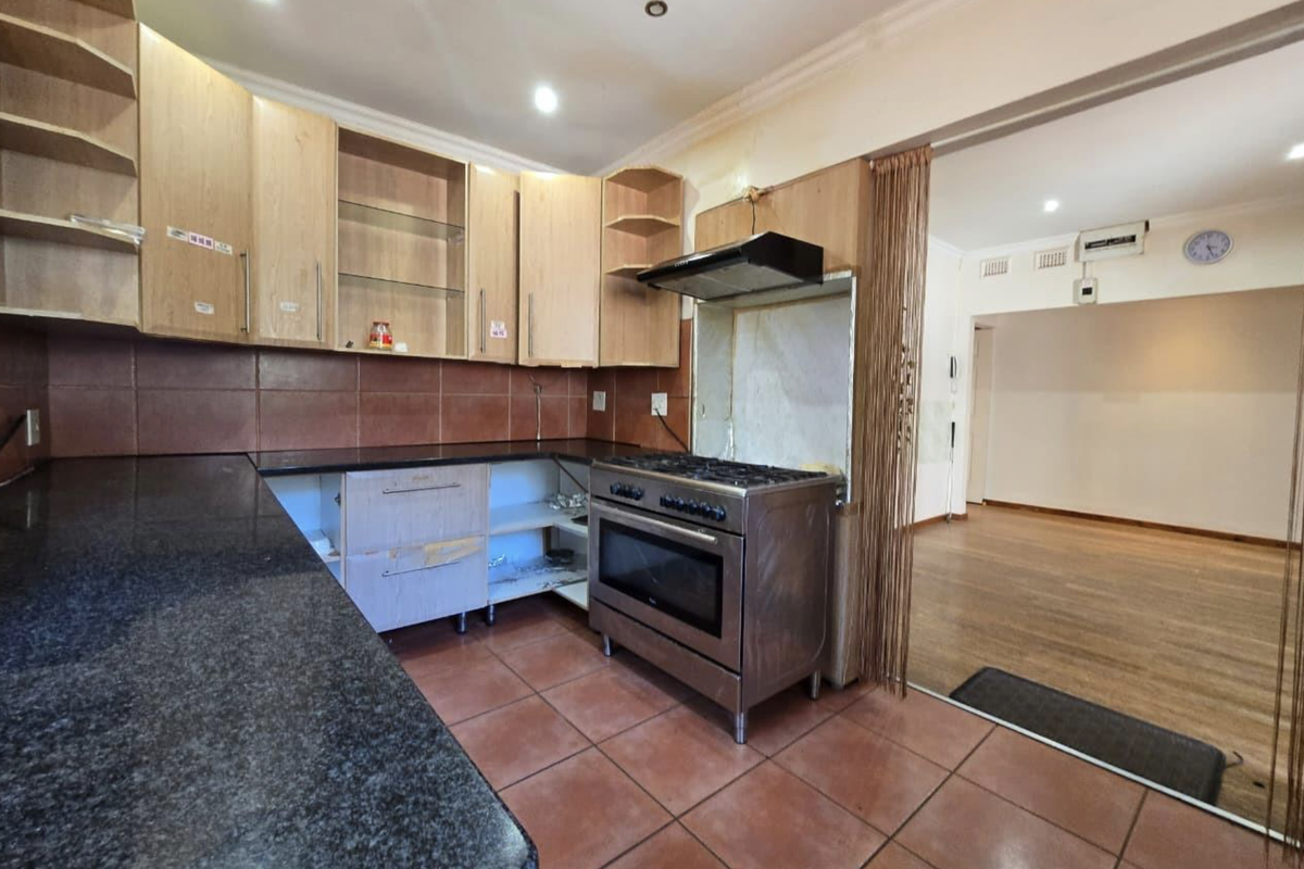 A dated kitchen featuring granite countertops, tiled flooring, and a freestanding stove, currently requiring cosmetic updates and cabinet repairs.