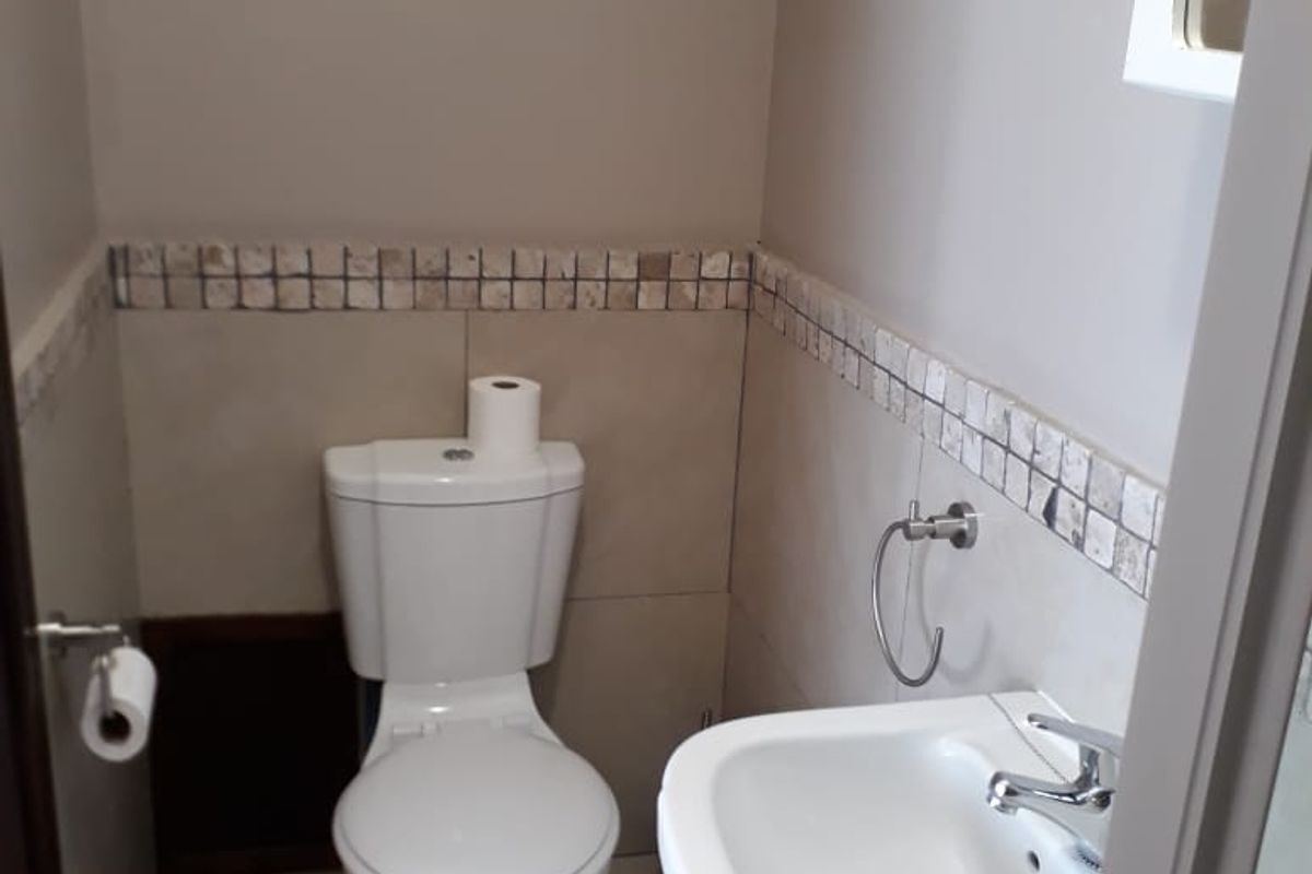 A compact guest bathroom featuring a pedestal sink, a standard toilet, and decorative mosaic tile accents along the walls.