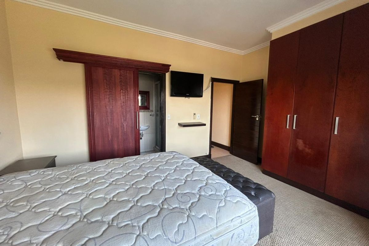 Spacious bedroom featuring built-in wooden cabinetry, a sliding door leading to an en-suite bathroom, and neutral wall finishes.