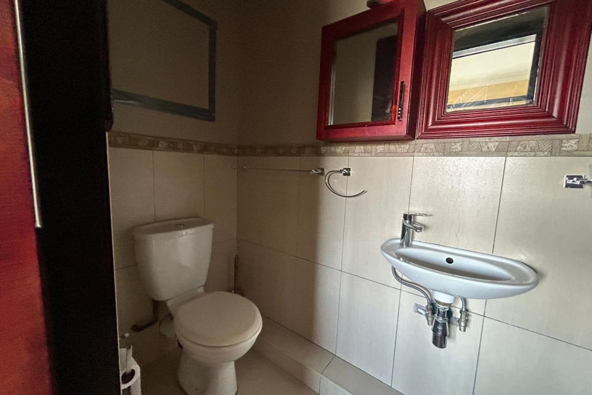 A compact bathroom featuring a wall-mounted basin, a standard toilet, and decorative wall tiling with built-in cabinetry.
