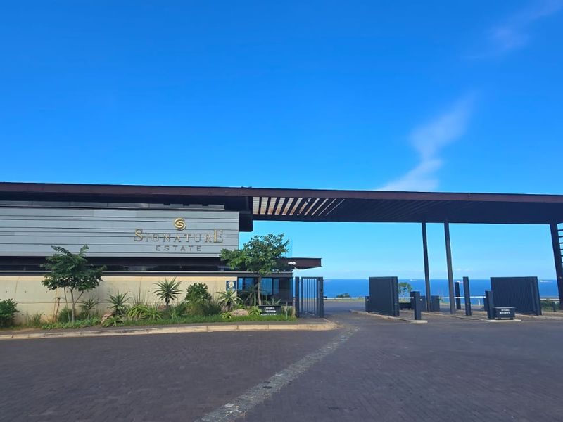 The main entrance and security gatehouse of the Signature Estate, featuring modern architectural design, paved driveway, and landscaped surroundings with ocean views.