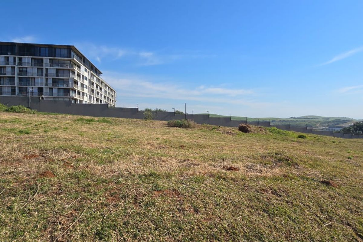 A vacant residential plot featuring a gentle slope, perimeter boundary wall, and views of the surrounding neighbourhood and nearby apartment complex.