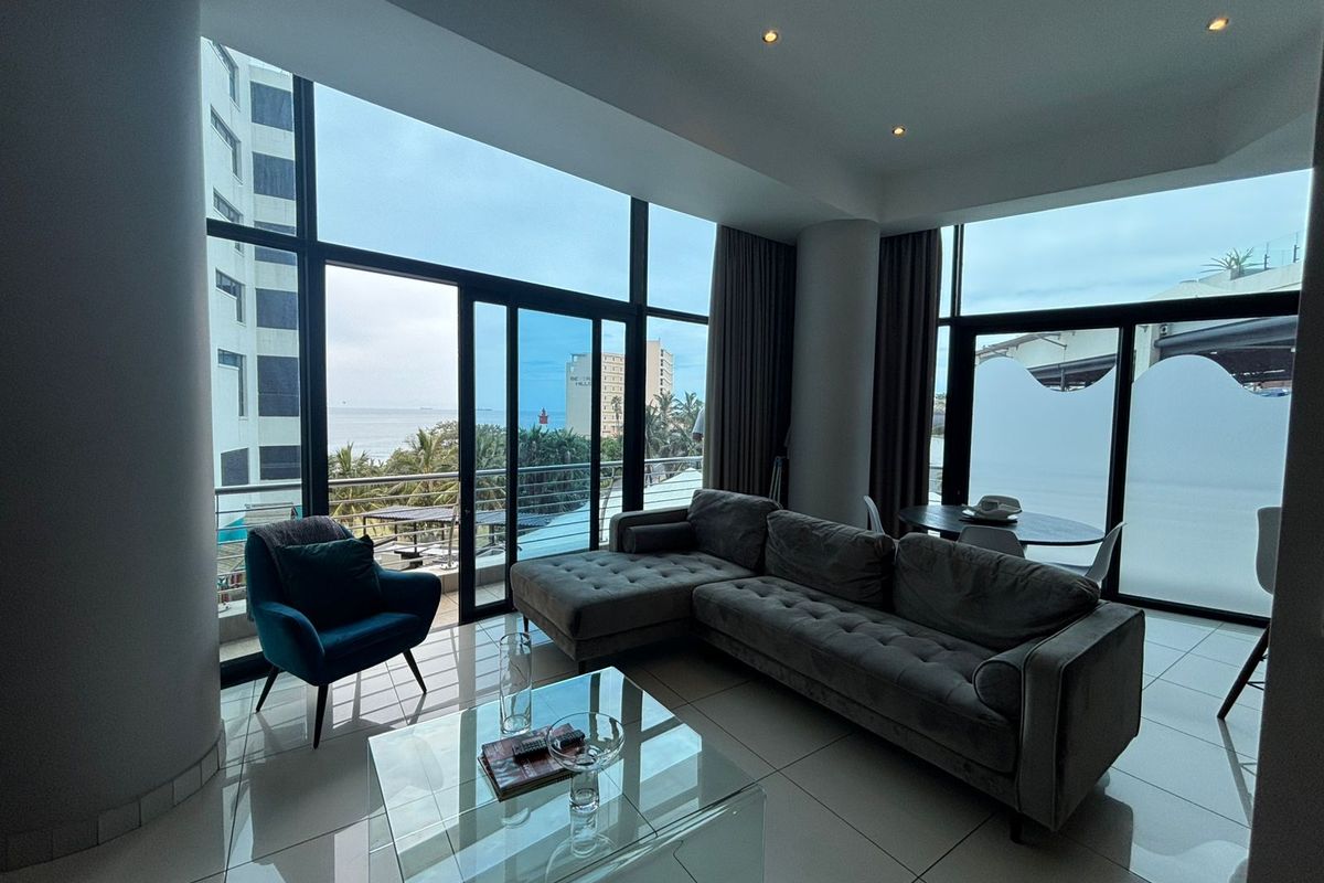 Spacious living area featuring floor-to-ceiling windows, tiled flooring, and direct access to a balcony with coastal views.