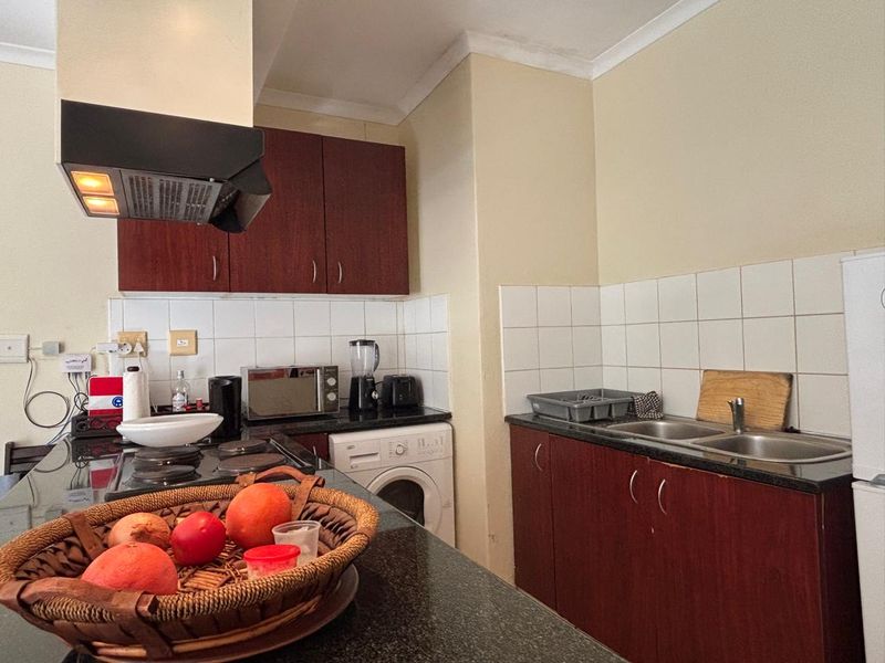 Functional kitchen featuring dark wood cabinetry, granite countertops, a built-in hob with extractor fan, and a double sink with tiled backsplash.