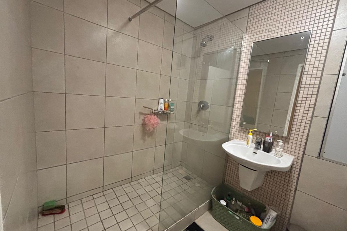 A functional bathroom featuring a glass-enclosed shower, wall-mounted basin, and neutral wall tiling.