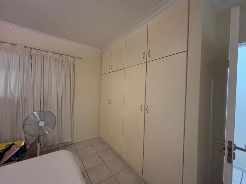 A bedroom featuring extensive floor-to-ceiling built-in cupboards, tiled flooring, and neutral wall finishes.