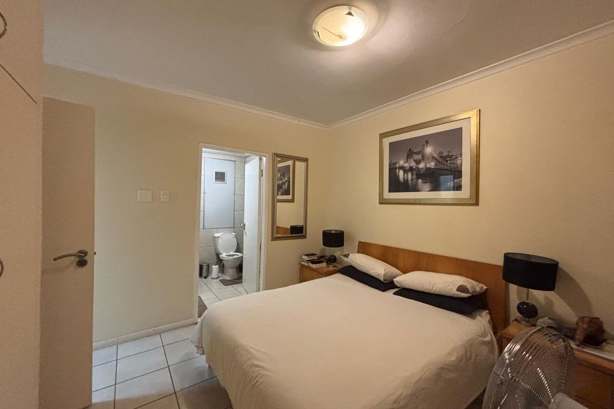 A bedroom featuring tiled flooring, a built-in cupboard, and an attached en-suite bathroom with a toilet.