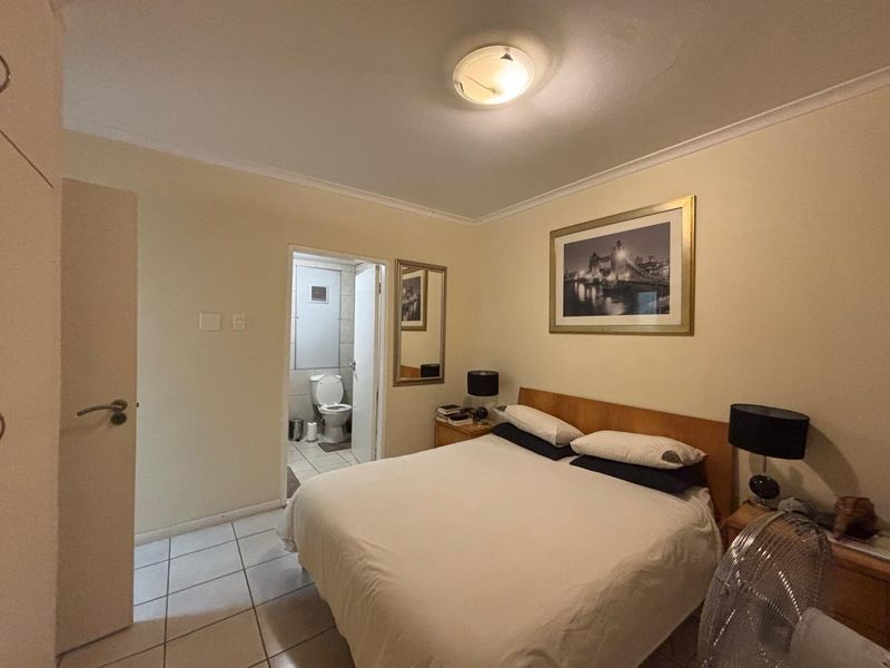A bedroom featuring tiled flooring, a built-in cupboard, and an attached en-suite bathroom with a toilet.