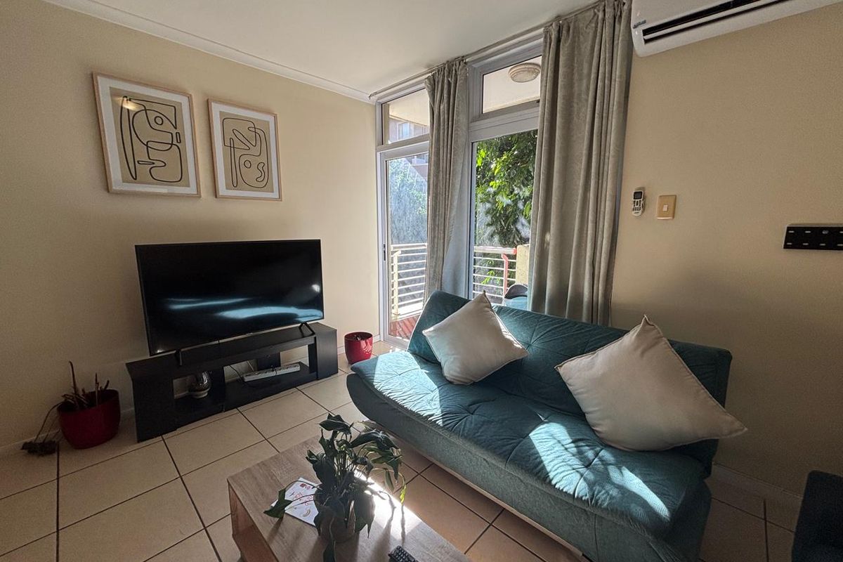 A compact living room featuring tiled flooring, a wall-mounted air conditioning unit, and a sliding glass door providing access to an outdoor area.